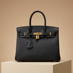 Black handbag with gold hardware on a beige pedestal against a beige background